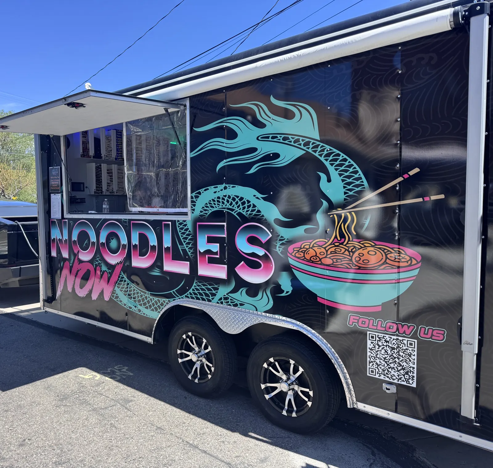 The Noodles Now trailer parked with the service window open, black wrap with a teal dragon and ramen bowl